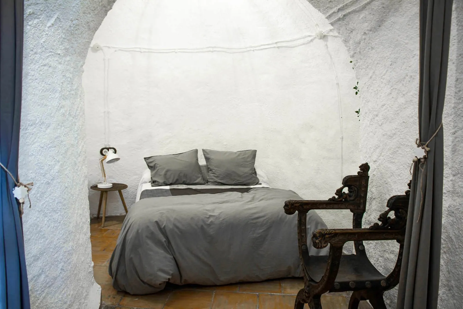 Dormitorio principal con cama de matrimonio y sillón de madera tallada dentro de la cueva
